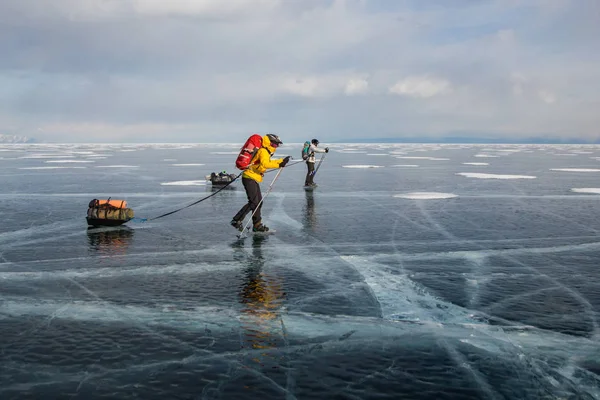 Два человека с рюкзаками проходят через поверхность ледяной воды и холмы на заднем плане, Россия, озеро Байкал — стоковое фото