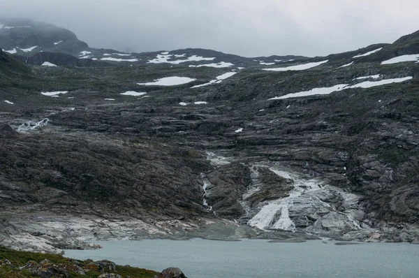 Lake on foot of rock with snow on surface, Norway, Hardangervidda National Park — Stock Photo