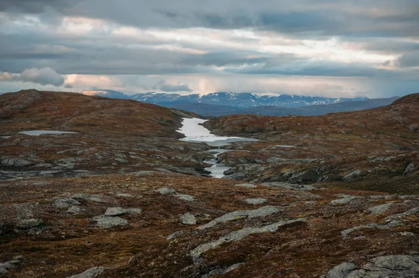 Campo con pequeños estanques de agua y montañas en el fondo durante el clima tormentoso, Noruega, Parque Nacional Hardangervidda - foto de stock