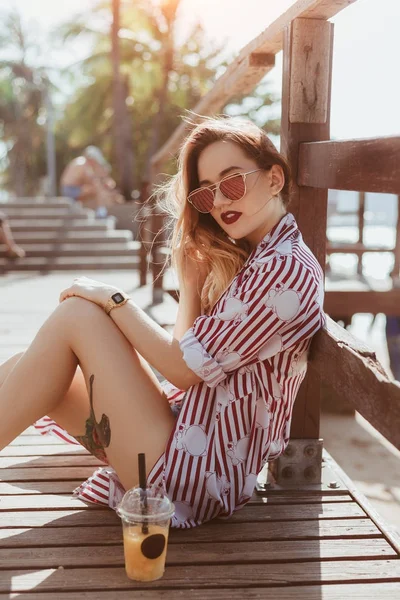 Side view of beautiful young woman sitting on floor of wooden pier — Stock Photo