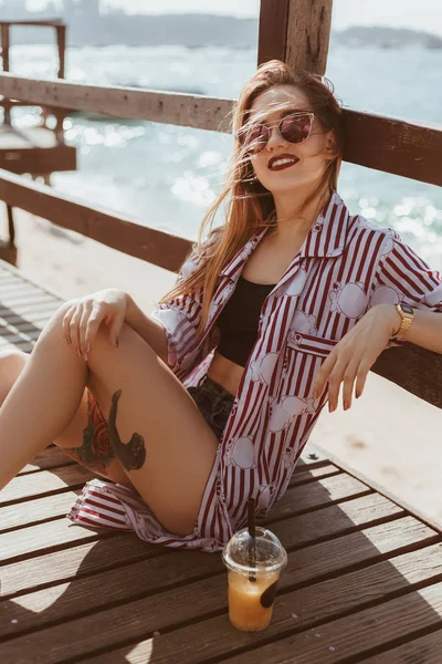 Atraente jovem mulher sentada no chão do cais na praia — Fotografia de Stock