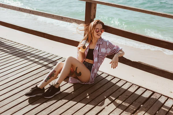 Giovane donna con tazza di plastica seduta sul molo di legno in spiaggia — Foto stock