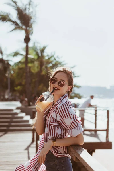 Sorridente giovane donna bere cocktail sul molo — Foto stock