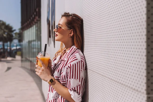 Seitenansicht der attraktiven jungen Frau mit Cocktail im Plastikbecher lehnt sich an die Wand — Stockfoto