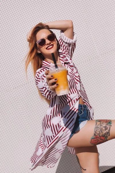 Beautiful young woman with plastic cup of cocktail leaning back on white wall — Stock Photo