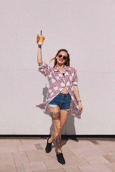 Smiling woman holding plastic cup of cocktail in front of white wall — Stock Photo