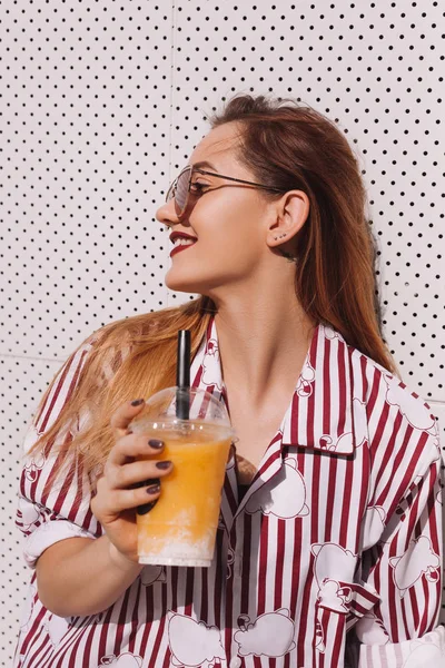 Sensual woman with plastic cup of refreshing cocktail leaning back on white wall — Stock Photo