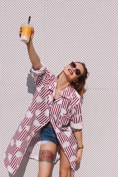 Hermosa mujer joven sosteniendo cóctel en taza de plástico en frente de la pared blanca - foto de stock