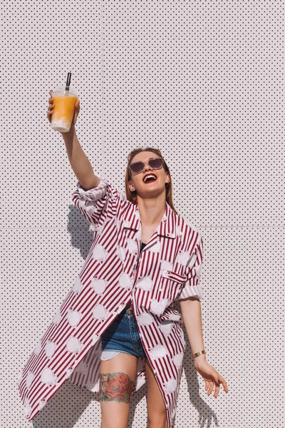 Attraente giovane donna che tiene cocktail in tazza di plastica davanti alla parete bianca — Foto stock