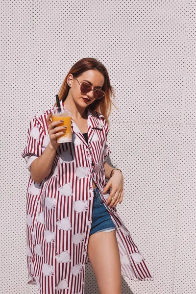 Hermosa mujer joven con camisa roja a rayas con batido de mango en taza de plástico - foto de stock