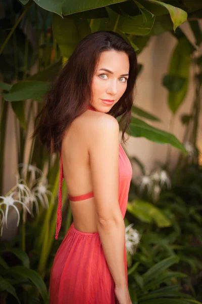 Bela jovem mulher em vestido na frente de plantas tropicais olhando para a câmera — Fotografia de Stock