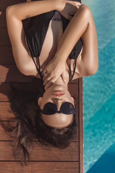 Von oben: attraktive junge Frau im schwarzen Badeanzug am Pool liegend — Stockfoto