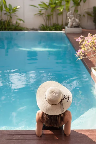 Vista para trás da jovem mulher em maiô e chapéu sentado na piscina do hotel — Fotografia de Stock