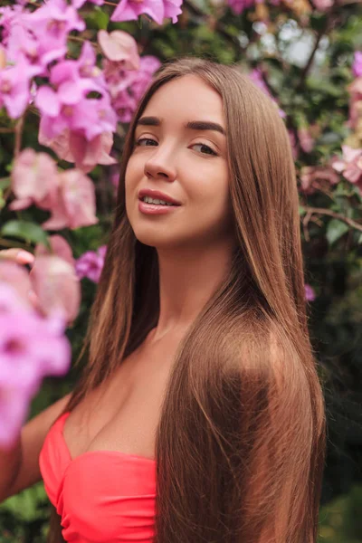 Portrait of beautiful young girl posing at pink flowers — Stock Photo