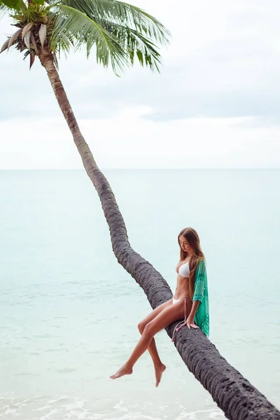 Молода дівчина в бікіні сидить на пальмі над океаном — стокове фото