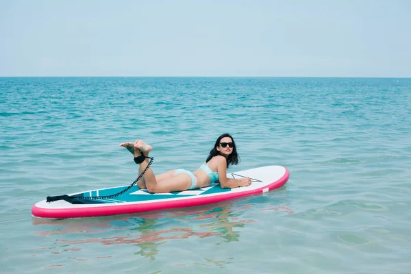 Attraktives schlankes Mädchen liegt im Tropenresort auf dem Paddelbrett auf dem Meer — Stockfoto