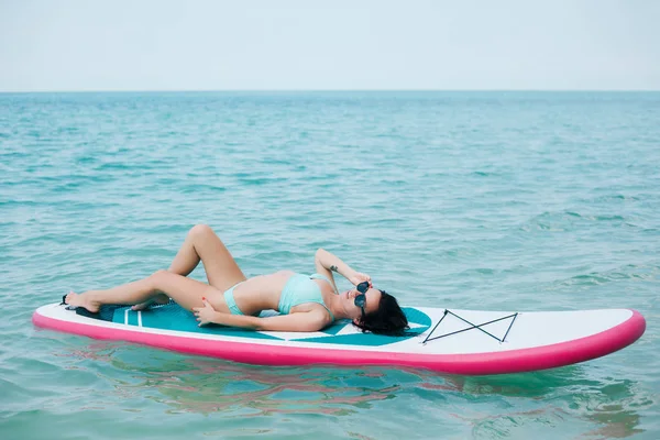 Junges schlankes Mädchen liegt auf dem Paddelbrett auf See in tropischem Resort — Stockfoto