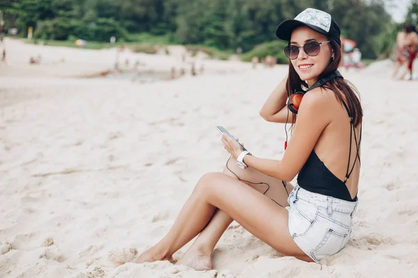 Donna attraente utilizzando smartphone ascoltare musica con le cuffie in spiaggia — Foto stock