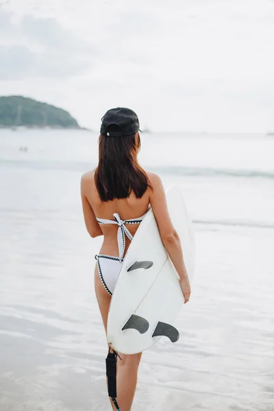 Вид сзади девушки в бикини, держащей доску для серфинга на пляже — стоковое фото