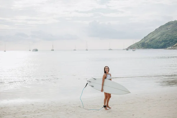 Young surfer in swimsuit walking with surfboard on beach at sea — Stock Photo