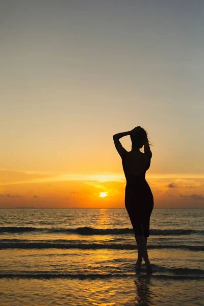 Rückansicht der Silhouette einer Frau, die bei Sonnenuntergang im Meer posiert — Stockfoto