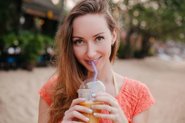 Feliz hermosa chica bebiendo cóctel en tropical resort y mirando a la cámara - foto de stock