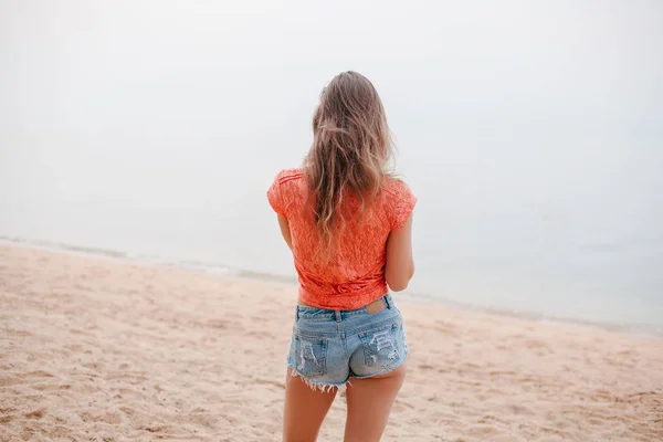 Vista trasera de la mujer de pie en pantalones cortos en la playa de arena - foto de stock