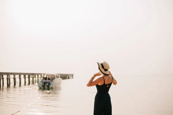 Vue arrière de la femme debout en robe et chapeau touchant sur la plage — Photo de stock