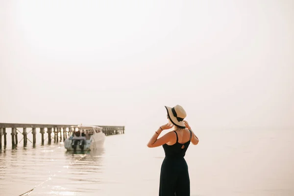 Vista posteriore della donna in piedi in abito e cappello toccante sulla spiaggia — Foto stock