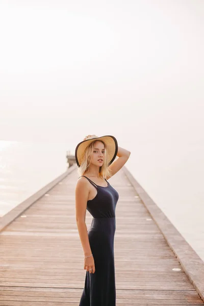Beautiful sensual woman in hat and dress looking at camera near ocean — Stock Photo