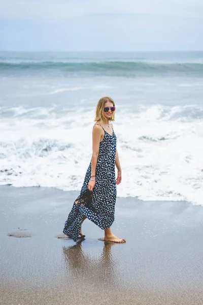 Hermosa chica rubia en vestido largo caminando cerca del océano - foto de stock