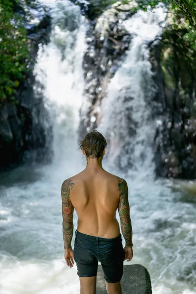 Rückseite tätowierter Mann mit heilendem Wasserfall im Hintergrund, Bali, Indonesien — Stockfoto