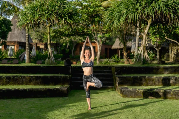 Femme attrayante pratiquant le yoga en pose d'arbre avec de belles plantes vertes sur fond, Bali, Indonésie — Photo de stock