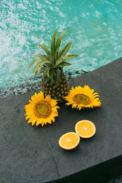 Vista close-up de abacaxi, laranja fatiada e belas flores amarelas na piscina — Fotografia de Stock