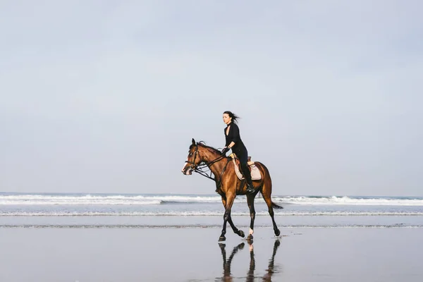 Young female equestrian riding horse on sandy beach — Stock Photo