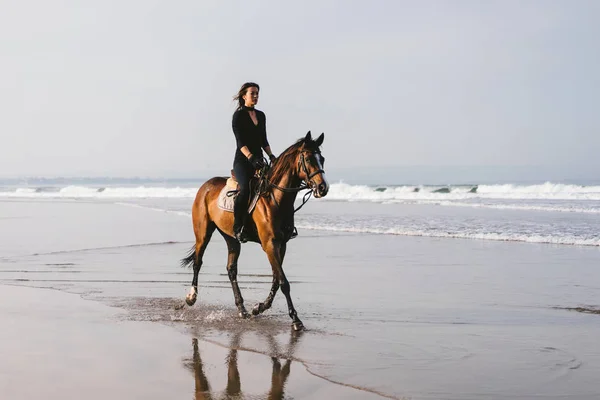 Jovem fêmea equestre cavalo de equitação perto do oceano ondulado — Fotografia de Stock