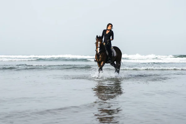 Вид спереду молода жінка верхи на коні у хвилястій воді — стокове фото