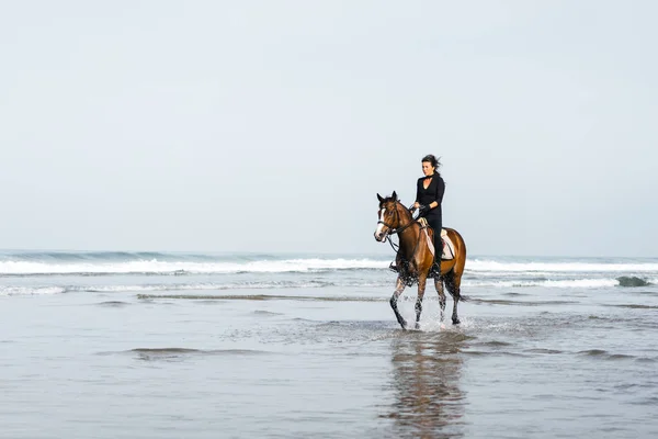 Female equestrian riding horse in wavy water — Stock Photo