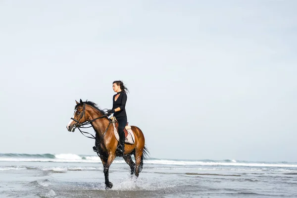 Jovem fêmea equestre equitação cavalo em água ondulada — Fotografia de Stock