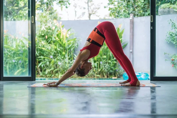 Vista lateral de la joven atlética practicando yoga en postura de perro boca abajo (Adho Mukha Svanasana) - foto de stock