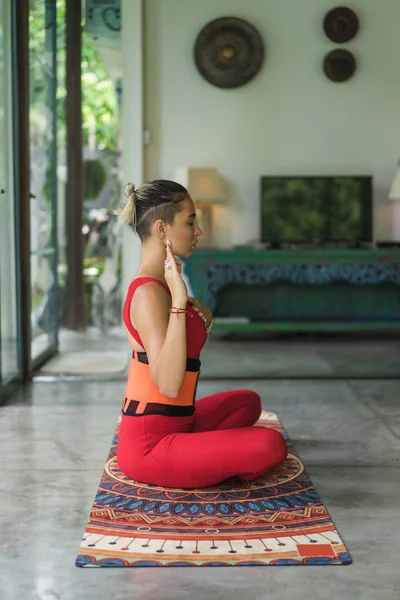 Vue latérale de belle jeune femme pratiquant le yoga en pose de lotus avec la main sur le cœur à la maison — Photo de stock