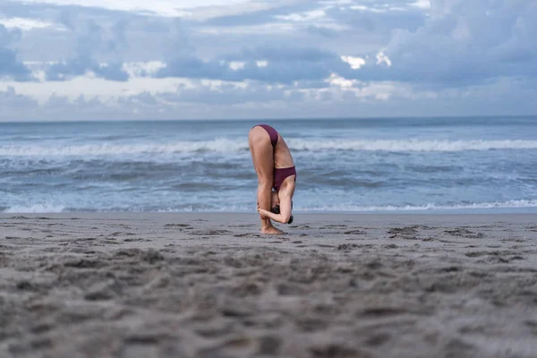 Вид збоку молода жінка йоги в стоячи вперед вигин представляють (Uttanasana) на березі моря — стокове фото