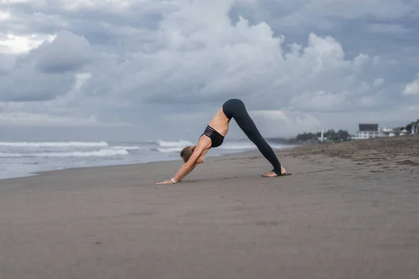 Junge Frau praktiziert Yoga in abwärts gerichteter Hundepose (adho mukha svanasana) an der Küste — Stockfoto