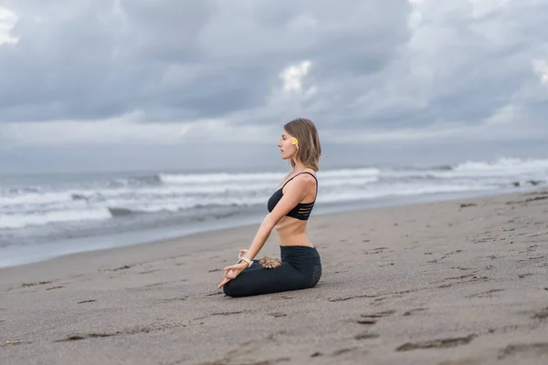 Young woman practicing yoga in lotus pose on seashore — Stock Photo