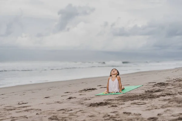 Niño pequeño y feliz practicando yoga en Upward-Facing Dog (Urdhva Mukha Svanasana) posan en la orilla del mar - foto de stock