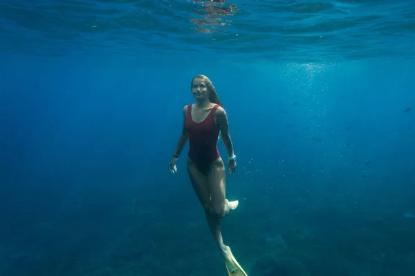 Foto submarina de una mujer joven en traje de baño y aletas buceando solo en el océano - foto de stock