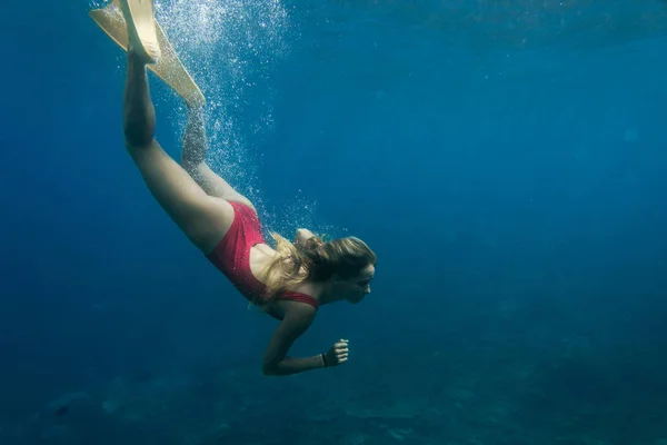 Подводное фото молодой женщины в купальнике и плавниках, ныряющей только в океане — стоковое фото