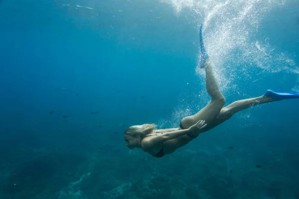 Vista lateral de la mujer en bikini y aletas buceando solo en el océano - foto de stock