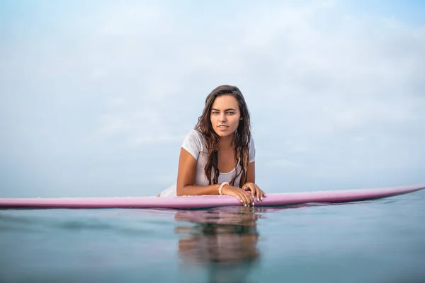 Attraktive junge Frau blickt auf Surfbrett im Meer in die Kamera — Stockfoto