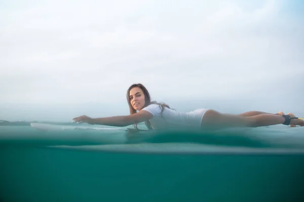 Jolie sportive en maillot de bain blanc nageant sur planche de surf dans l'océan — Photo de stock